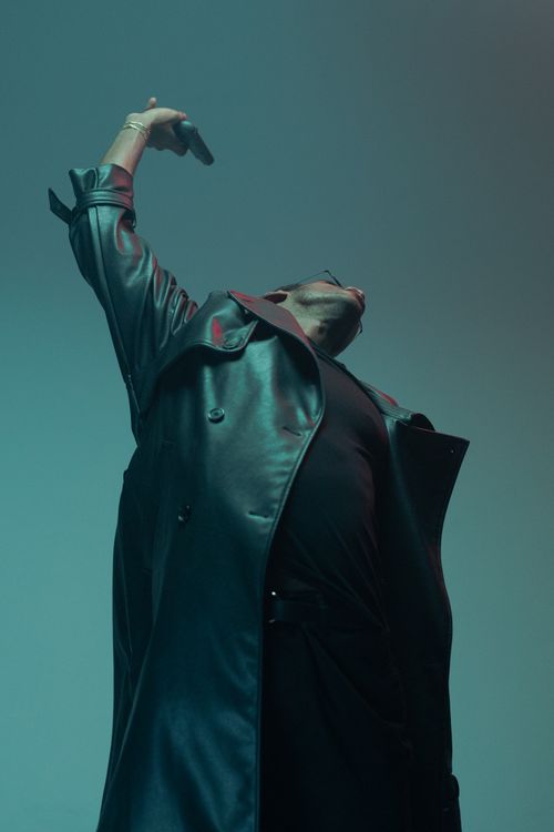 Free Low angle shot of a man in a trench coat posing dramatically with arm raised, stylish and bold. Stock Photo