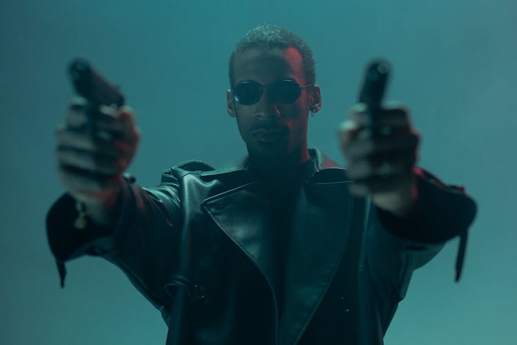 A Man In In Leather Coat Holding Handguns