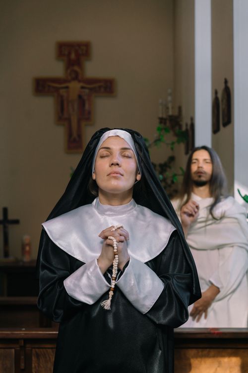 Free A nun stands indoors praying with a rosary, accompanied by another person in church. Stock Photo