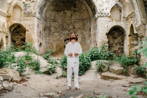 A Man in White Clothes Standing in the Ruins Holding Prayer Beads