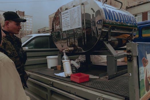 Military personnel at a mobile milk tank distribution point in an urban setting.