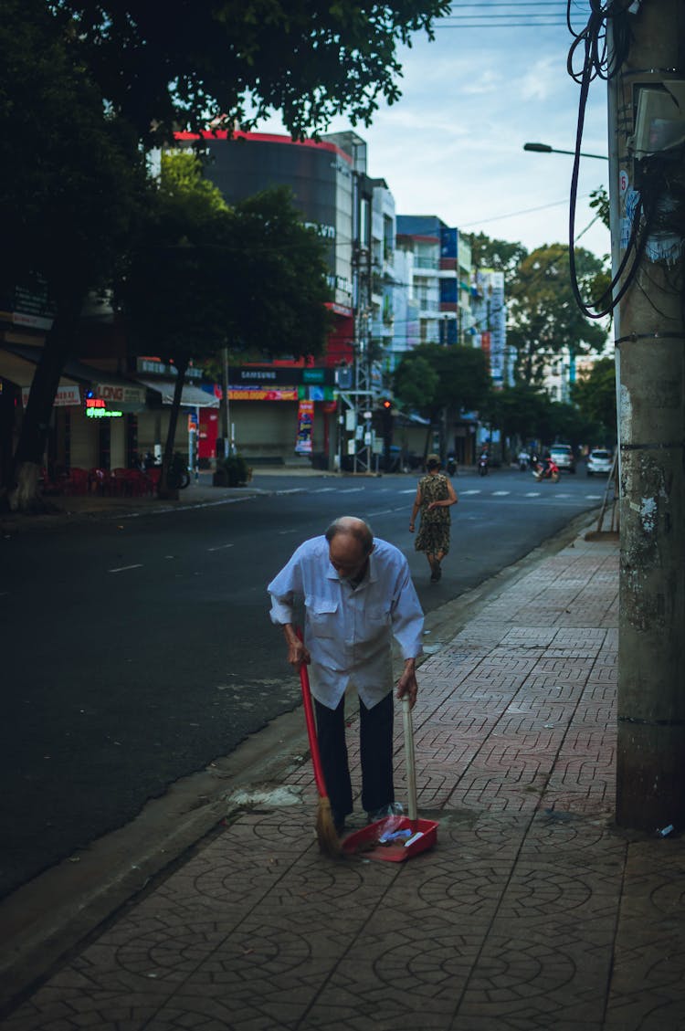 An Elderly Man Sweeping The Sidewalk