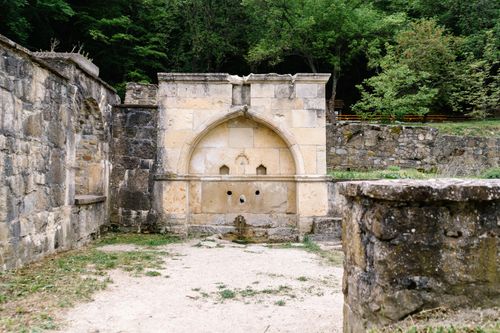Free An ancient stone fountain nestled in historic ruins surrounded by lush greenery outdoors. Stock Photo