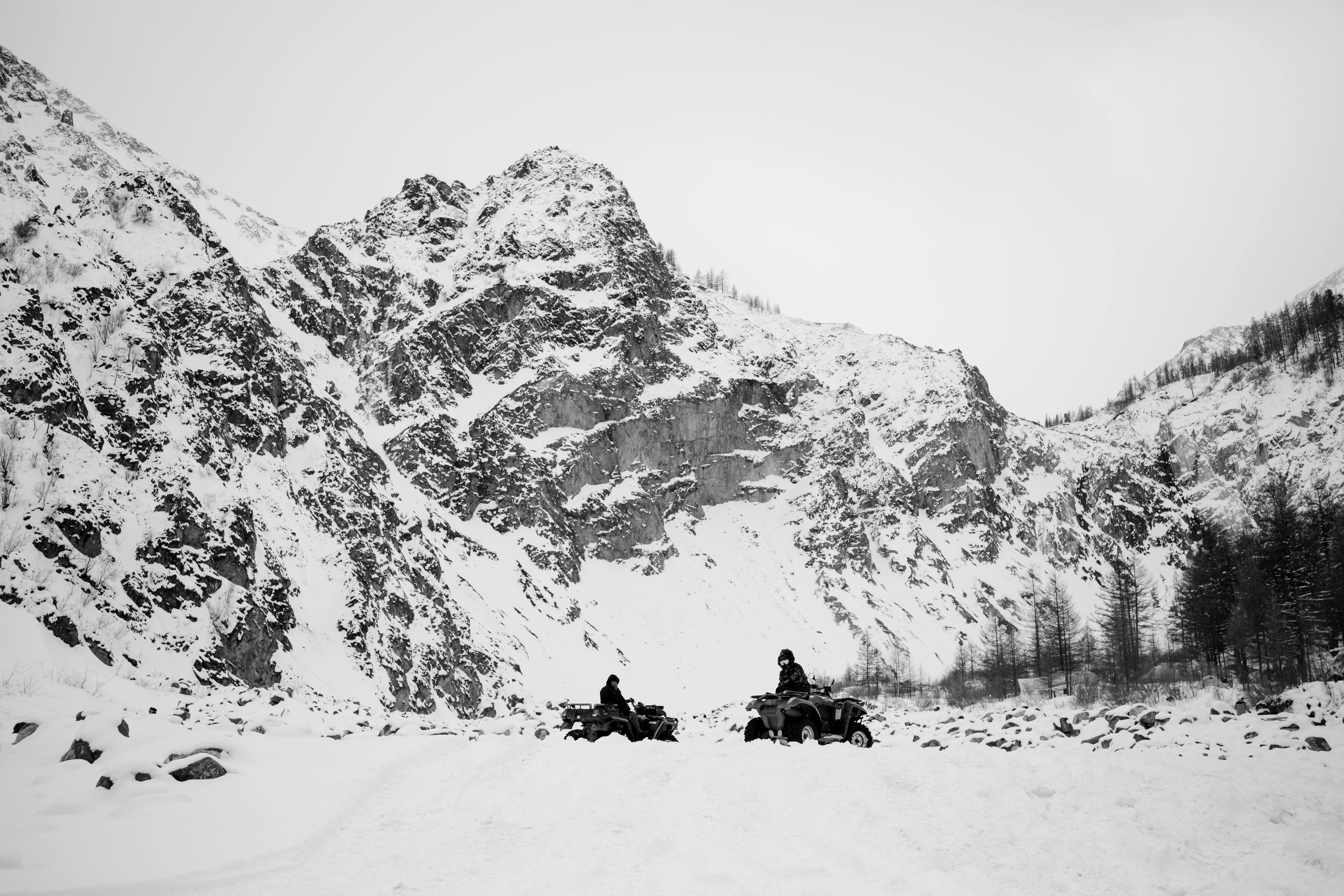 Riders traverse snow-covered mountains on ATVs, showcasing winter adventure.