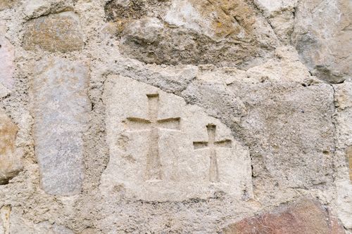 Free Close-up of a rustic stone wall with carved crosses, showcasing historical craftsmanship and texture. Stock Photo