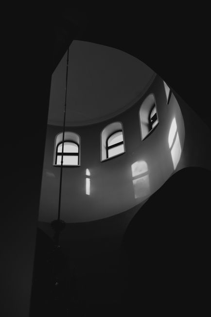 A striking black and white photo of arched windows casting shadows indoors, showcasing architectural elegance.