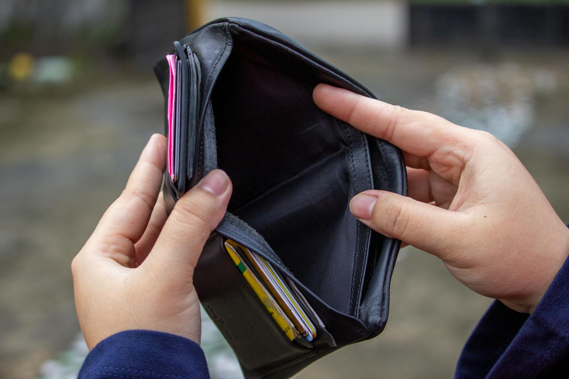 An outdoor image of hands holding an empty black wallet, suggesting financial scarcity.