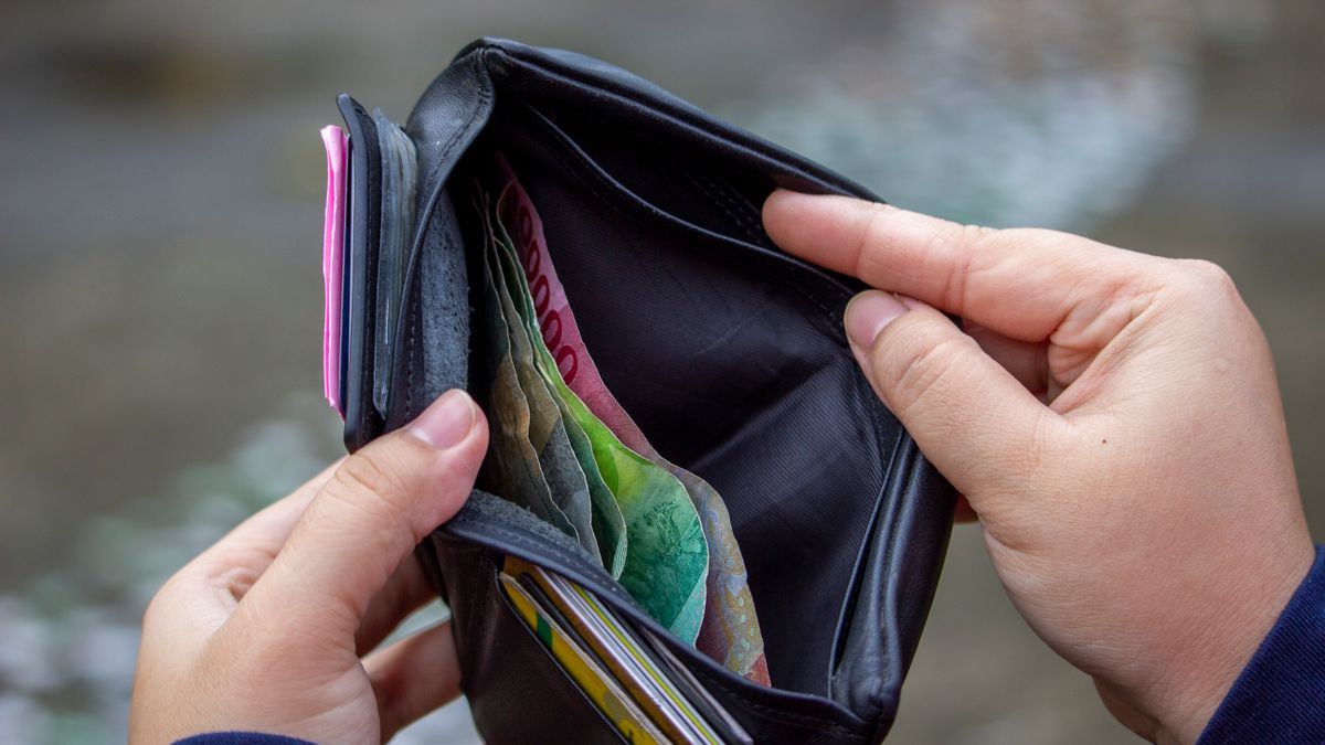 Person holding open wallet revealing banknotes, including Indonesian rupiah, in an outdoor setting.