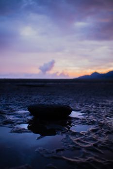 Stunning beach scene with a rock reflecting the purple sky at sunset.