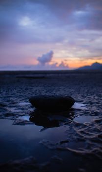 A tranquil beach scene with a stone reflecting the vibrant colors of a sunset, creating a serene atmosphere.