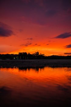 Vibrant orange sunset reflecting on a calm lake, showcasing silhouettes of trees under a dramatic sky.