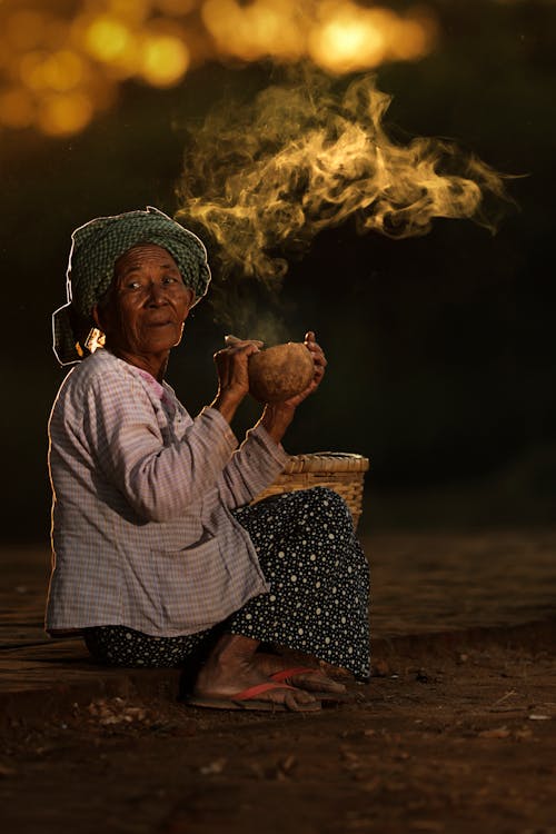 An Elderly Woman Wearing Headscarf While Smoking Tobacco