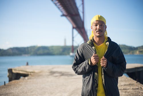 Man in Black Jacket and Yellow Knit Cap Standing Near Body of Water