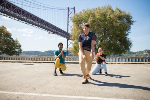 Free Three diverse adults dancing energetically outdoors under a Lisbon bridge on a sunny day. Stock Photo