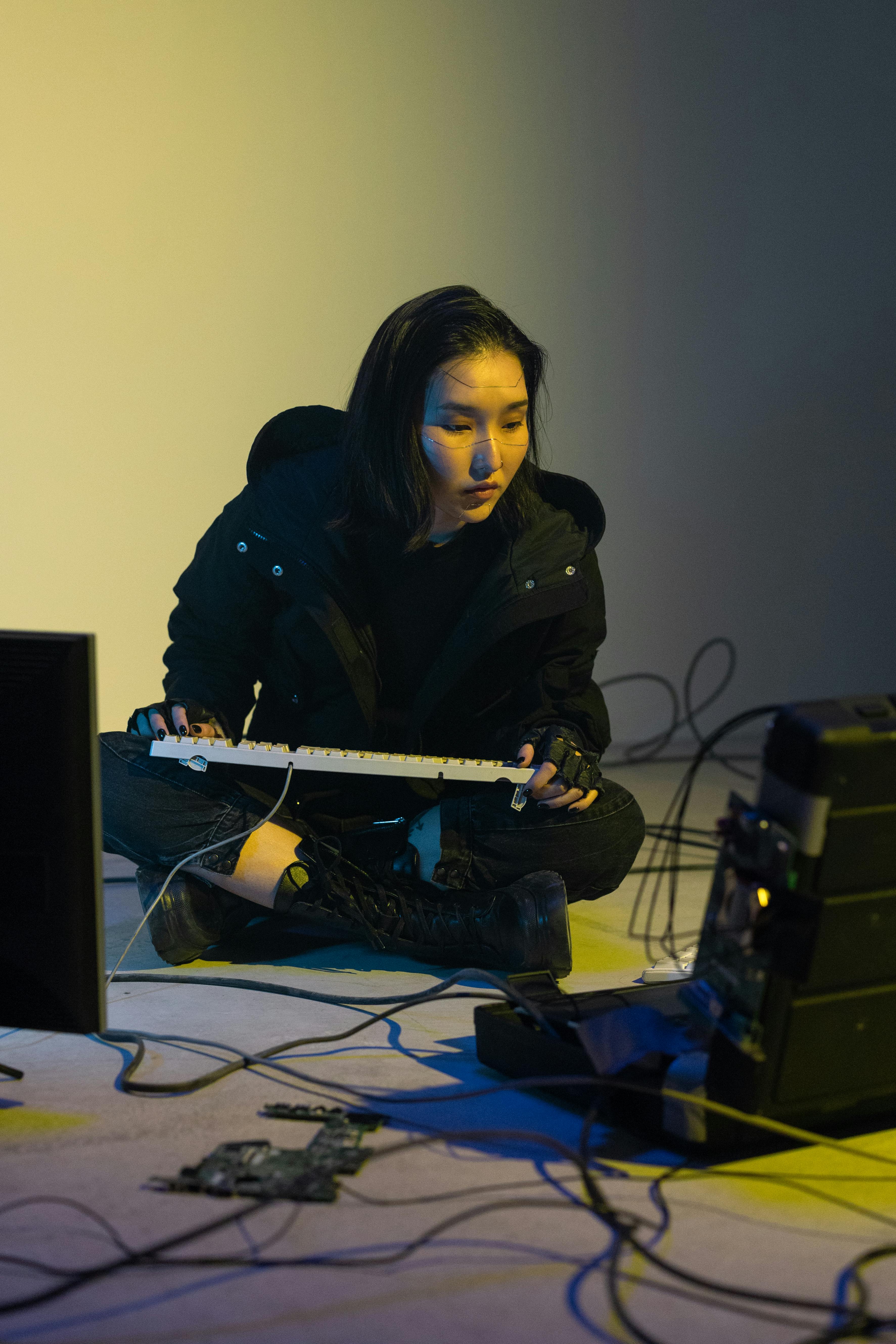 a woman in black jacket sitting on the floor while holding a computer keyboard