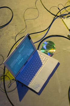 Top view of a laptop with cables and a CD on a concrete floor, highlighting technology and data concepts.