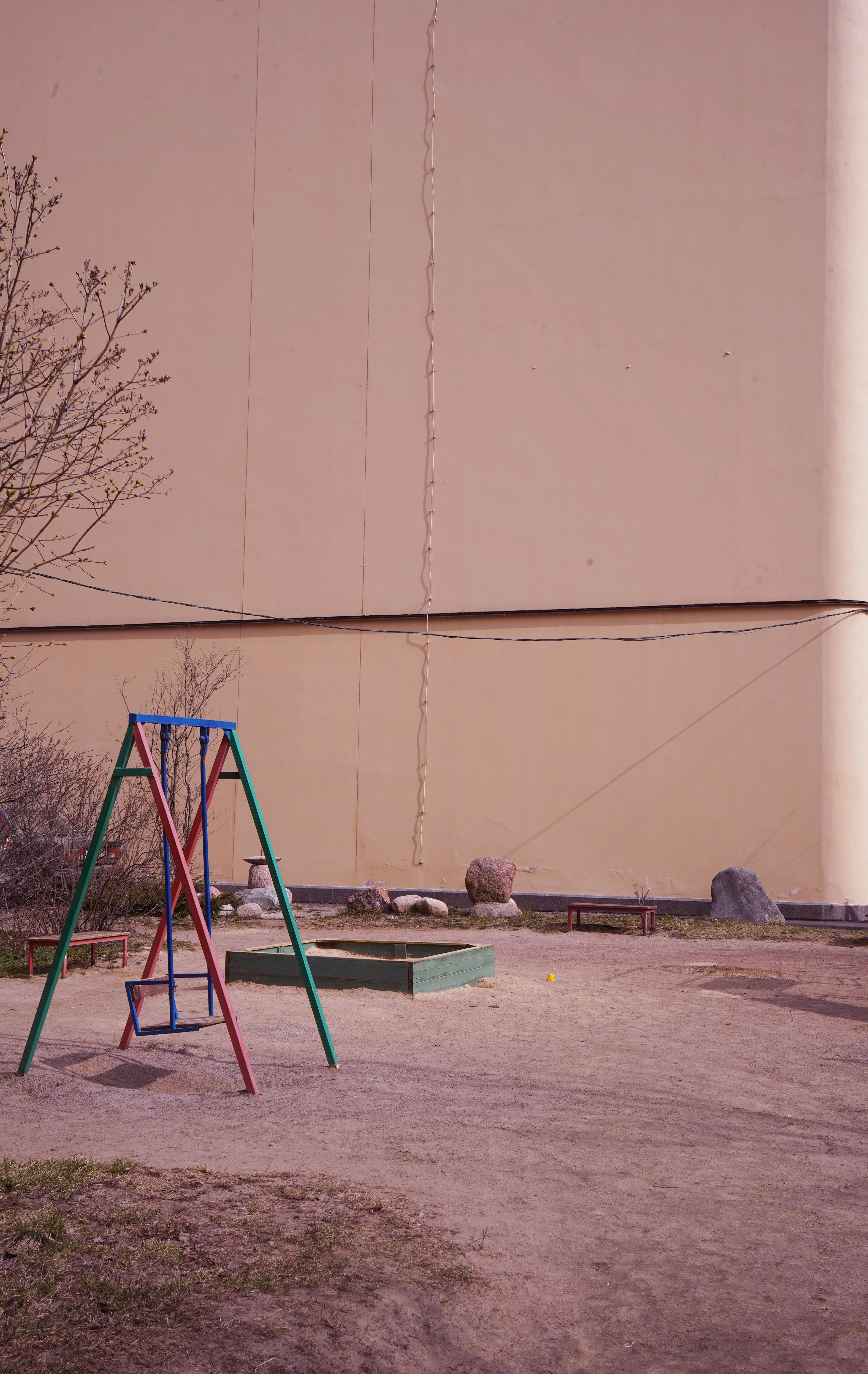 Deserted playground swing in front of a cracked concrete wall under clear daylight.
