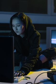 A woman in a dark room sits cross-legged, typing on a keyboard with a cyberpunk vibe.