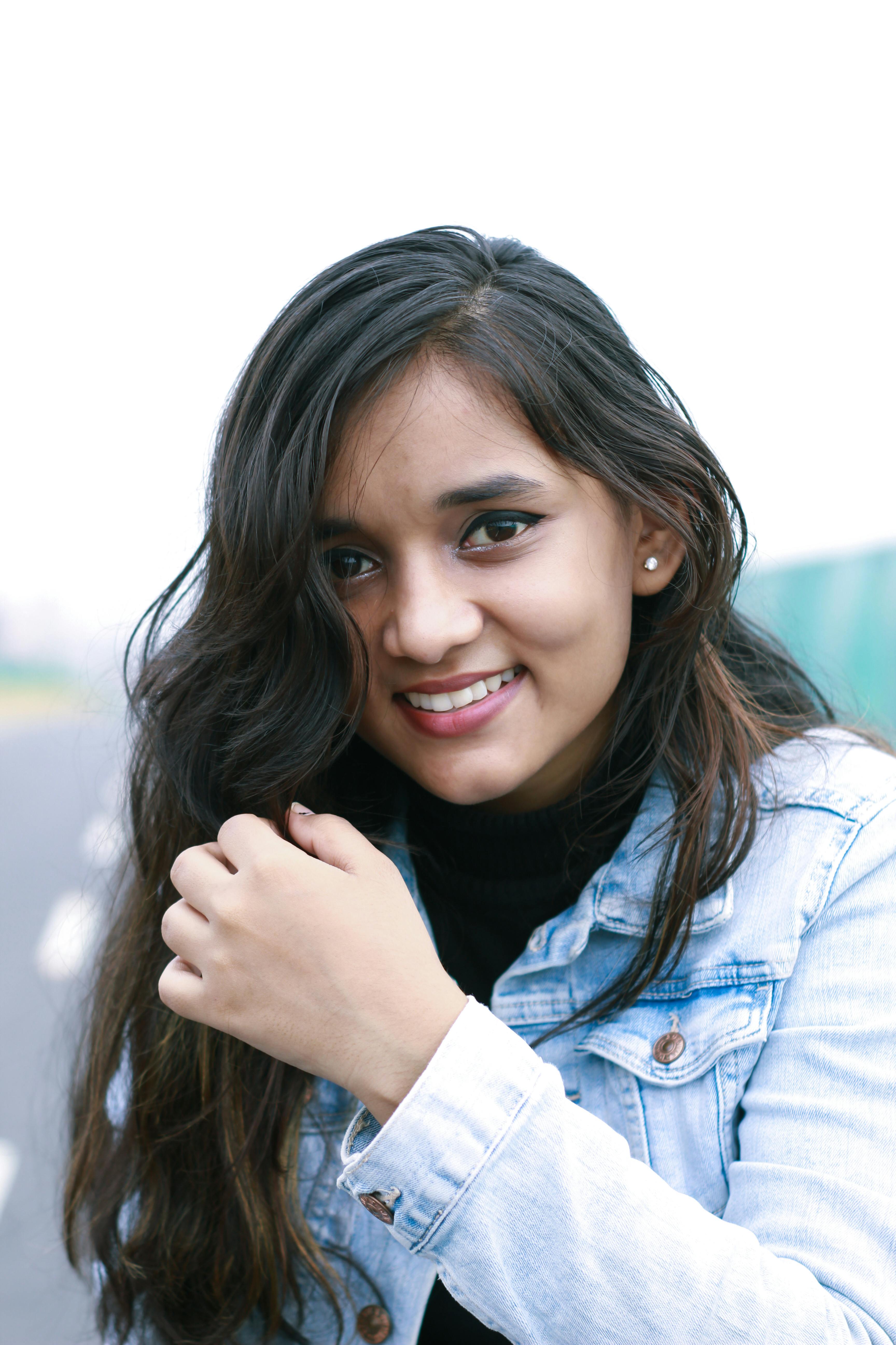 Close-up portrait of a smiling young woman in a denim jacket outdoors.