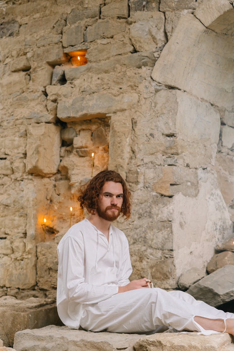 Man In White Clothes Holding Prayer Beads Sitting On A Rock