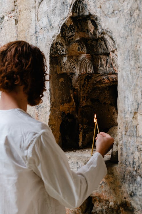 A Man in White Lighting a Candle in the Stone Wall Carving