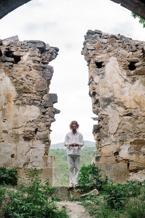 Man in White Clothing Standing in Ruins of a Building 