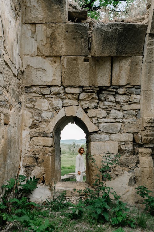 Man in White Clothing Standing near Ruins of a Building 