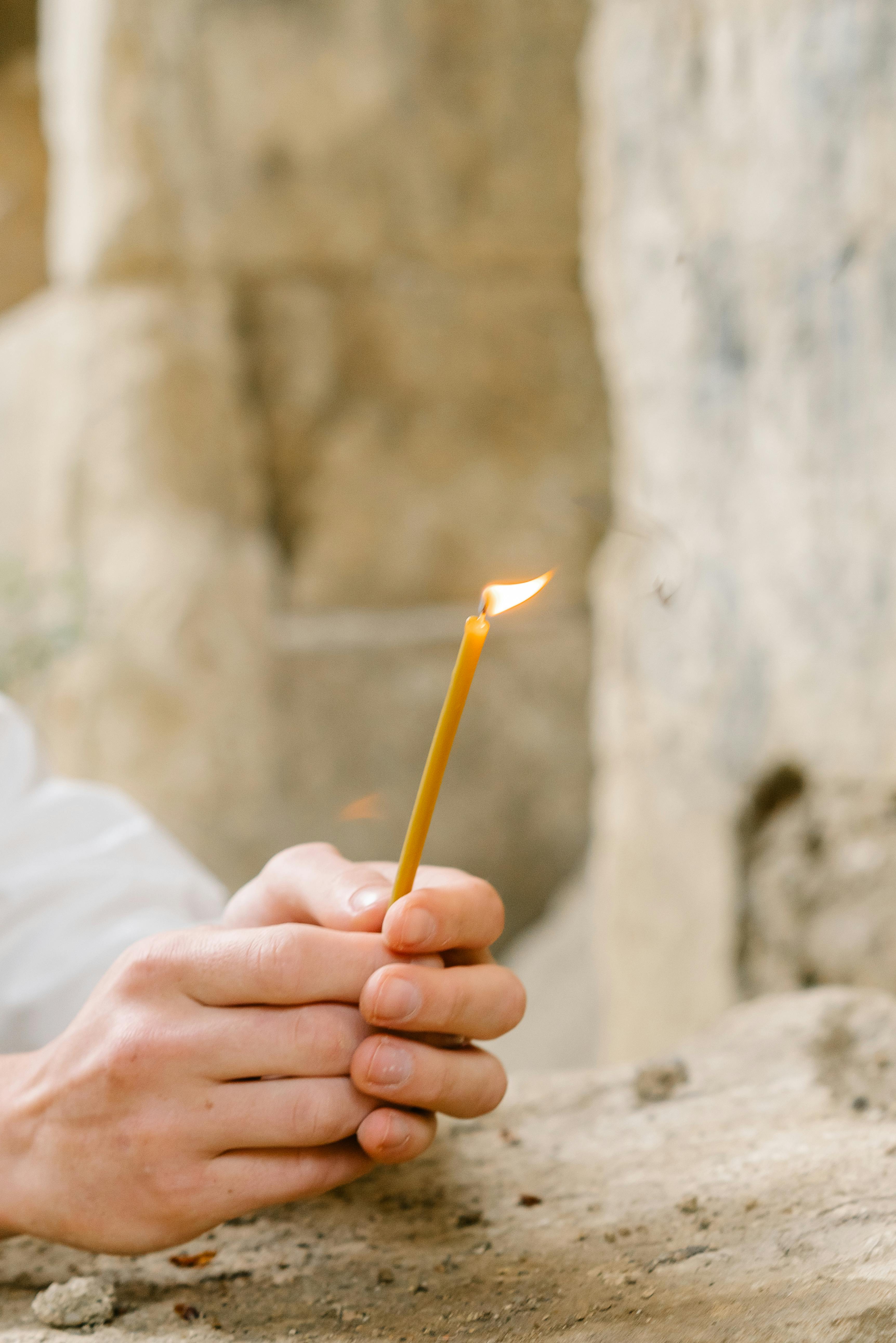 Detailed view of hands holding a lighted candle outdoors among stone textures.