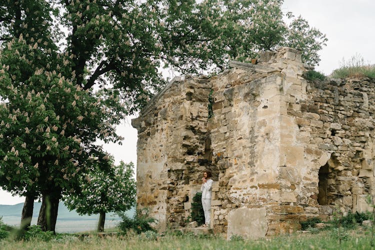 A Man  In White Clothes Standing On A Ruined Building With Hands Together