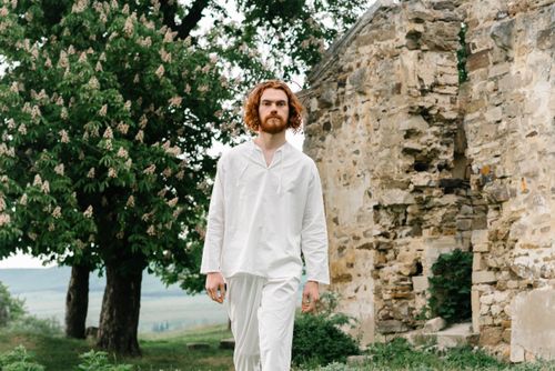 Free A bearded man in white clothes walks near an ancient stone wall and trees. Stock Photo