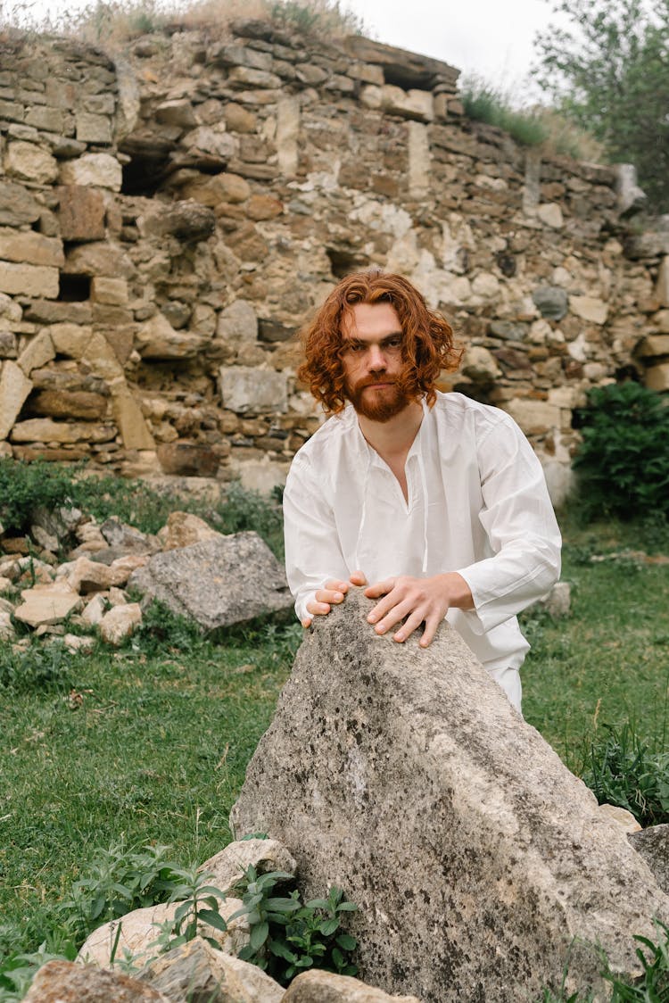 A Bearded Man In White Long Sleeves Holding On A Rock