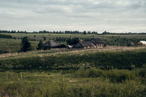 Free Rustic cottages nestled in a vast, lush rural landscape under a cloudy sky. Stock Photo