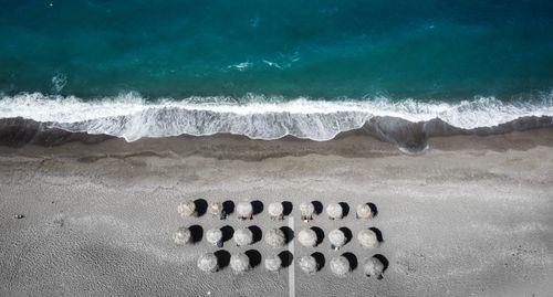 Free Aerial shot of a beach with straw umbrellas and serene ocean waves, perfect for summer. Stock Photo