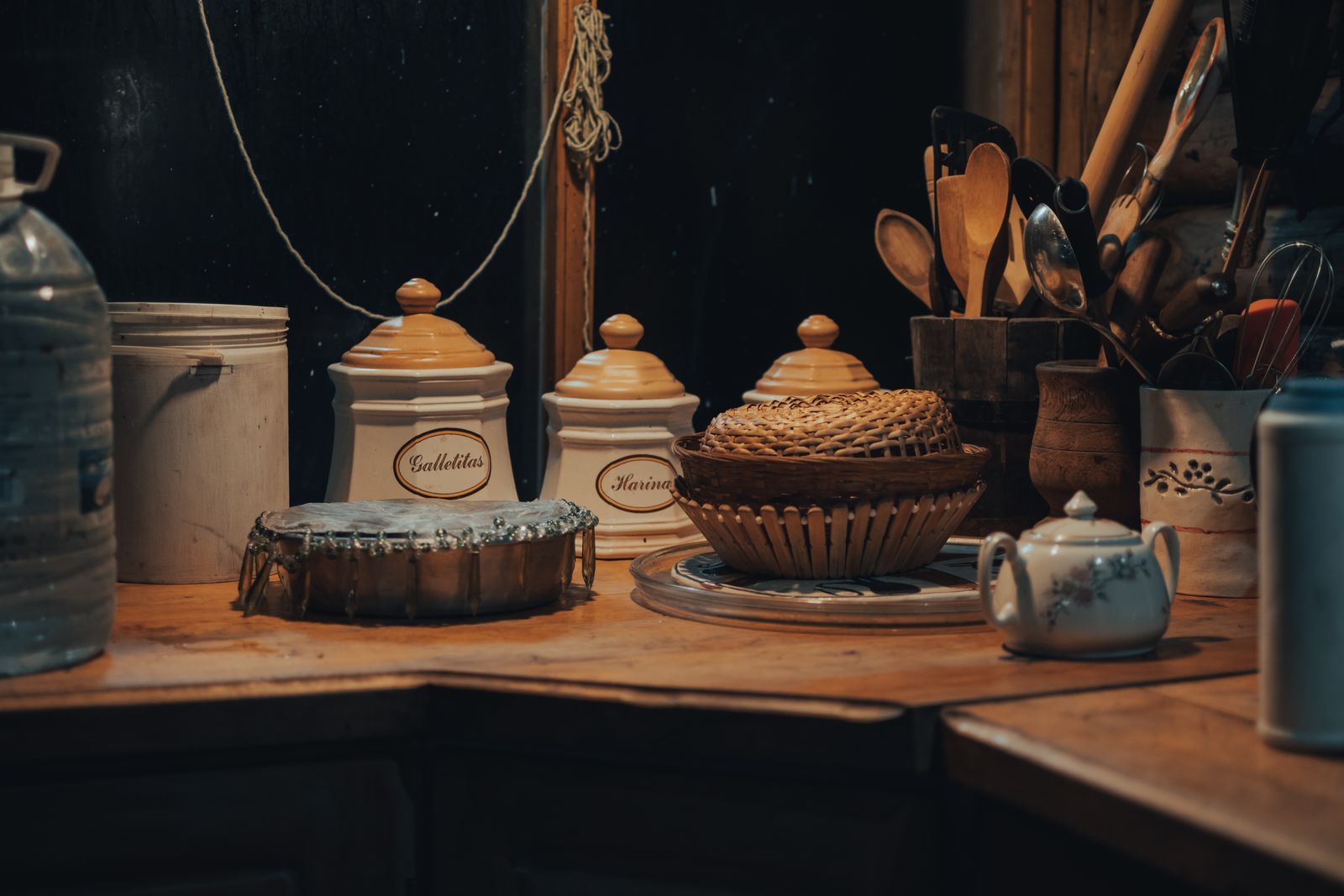 Cozy kitchen scene featuring wooden utensils, a teapot, and storage jars with warm lighting.