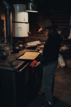 A woman in a cowboy hat bakes in a rustic kitchen environment, showcasing traditional cooking.