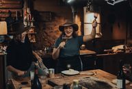 Two women enjoying wine and dancing in a rustic kitchen, wearing cowboy hats, filled with joy and laughter.
