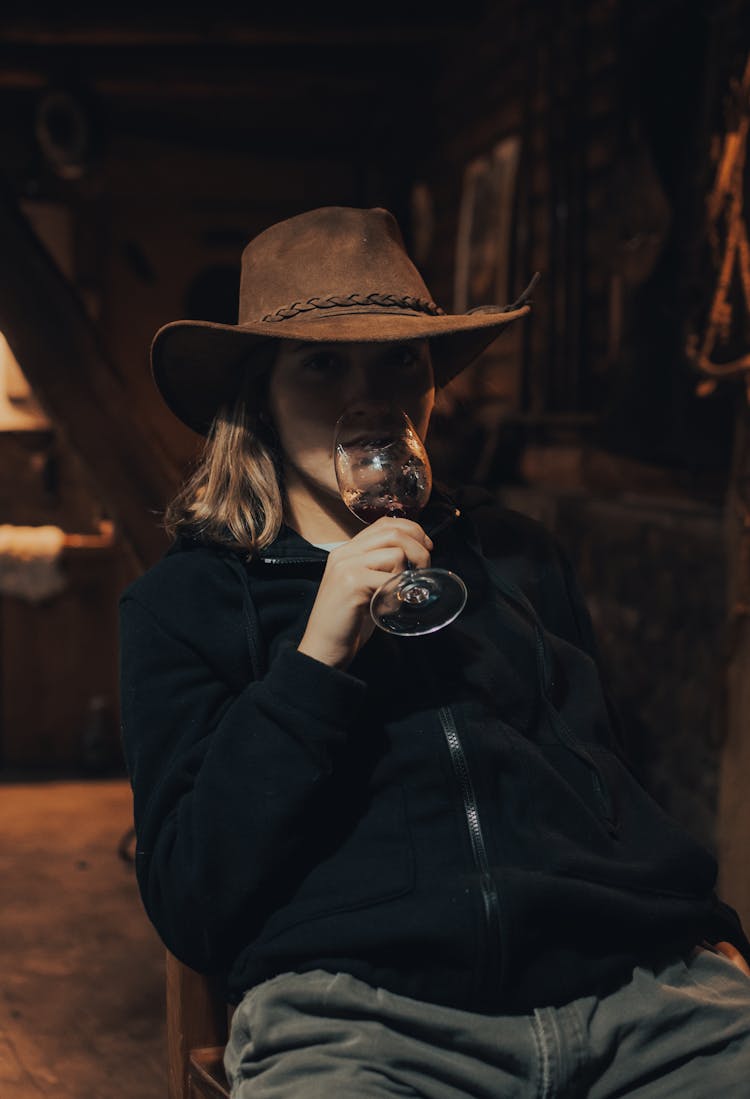 
A Woman In A Hat And A Jacket Drinking Wine