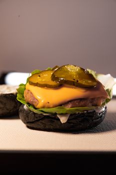 Close-up of a gourmet cheeseburger with pickles and black bun, highlighting fresh ingredients.