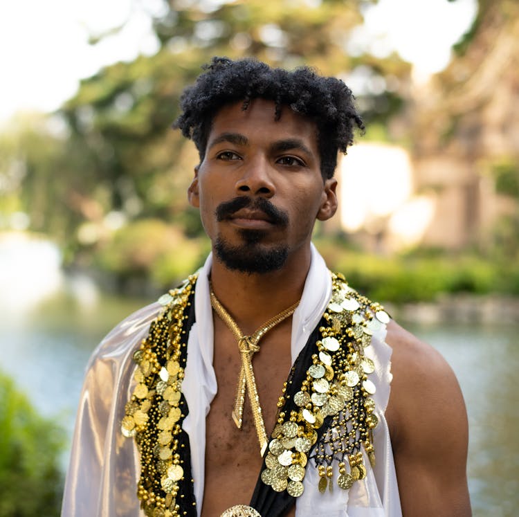 A Man Wearing A White Shirt With Black And Gold Embellishment