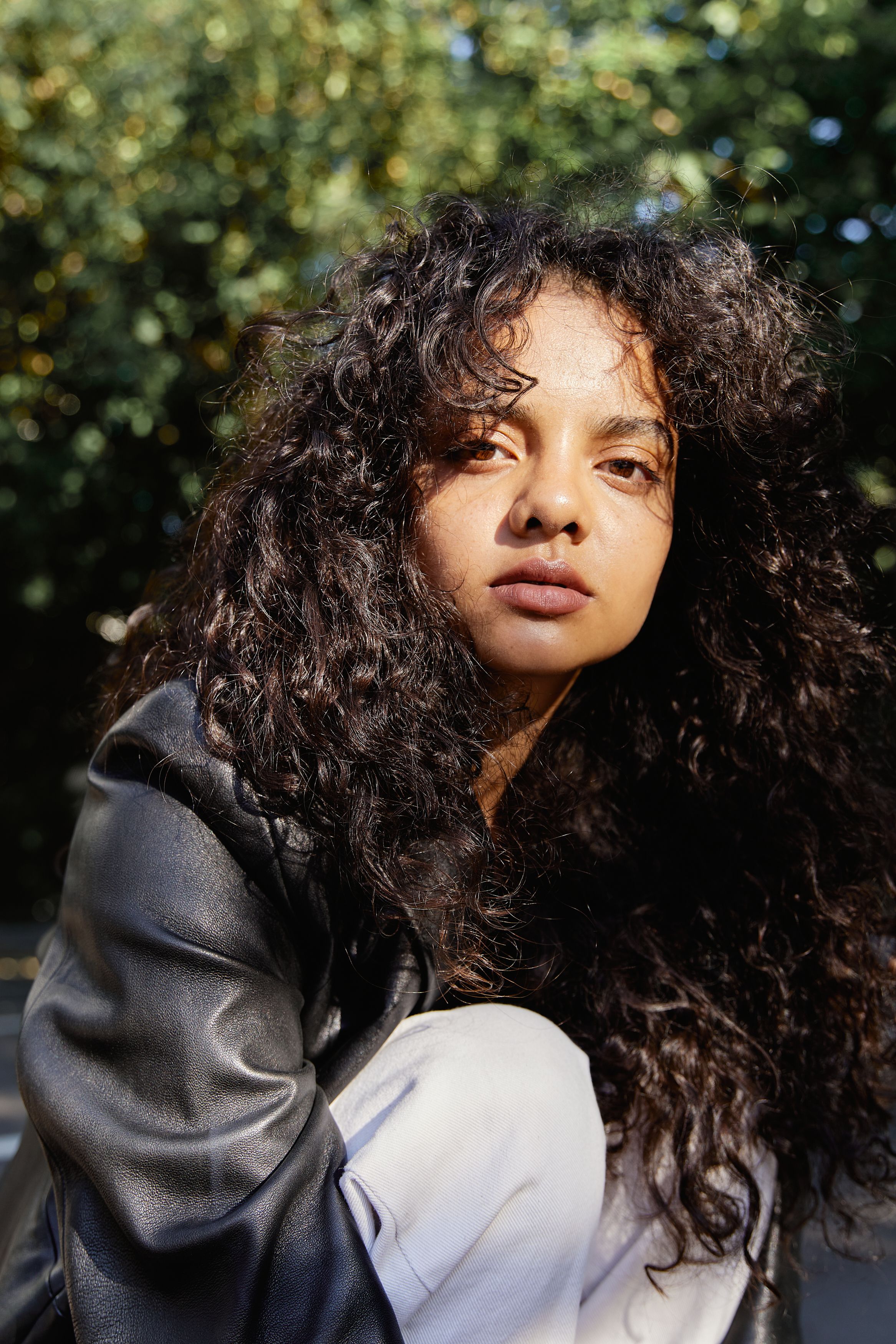 Close-up portrait of a woman with curly hair, wearing leather jacket, outdoors.