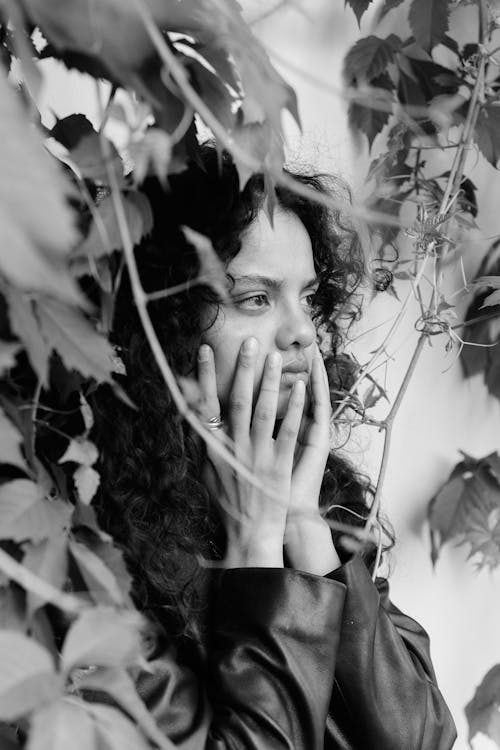 Grayscale Photo of a Woman Touching Her Face Near Vines