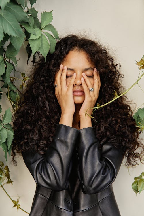 Photo of a Young Woman with Curly Hair, Wearing a Leather Jacket and Touching Her Face