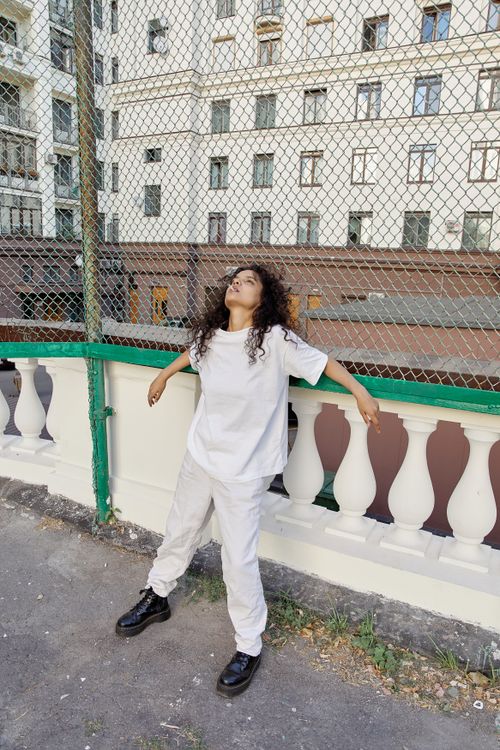 Free A young woman is leaning on a fence with a relaxed pose in an urban outdoor setting. Stock Photo