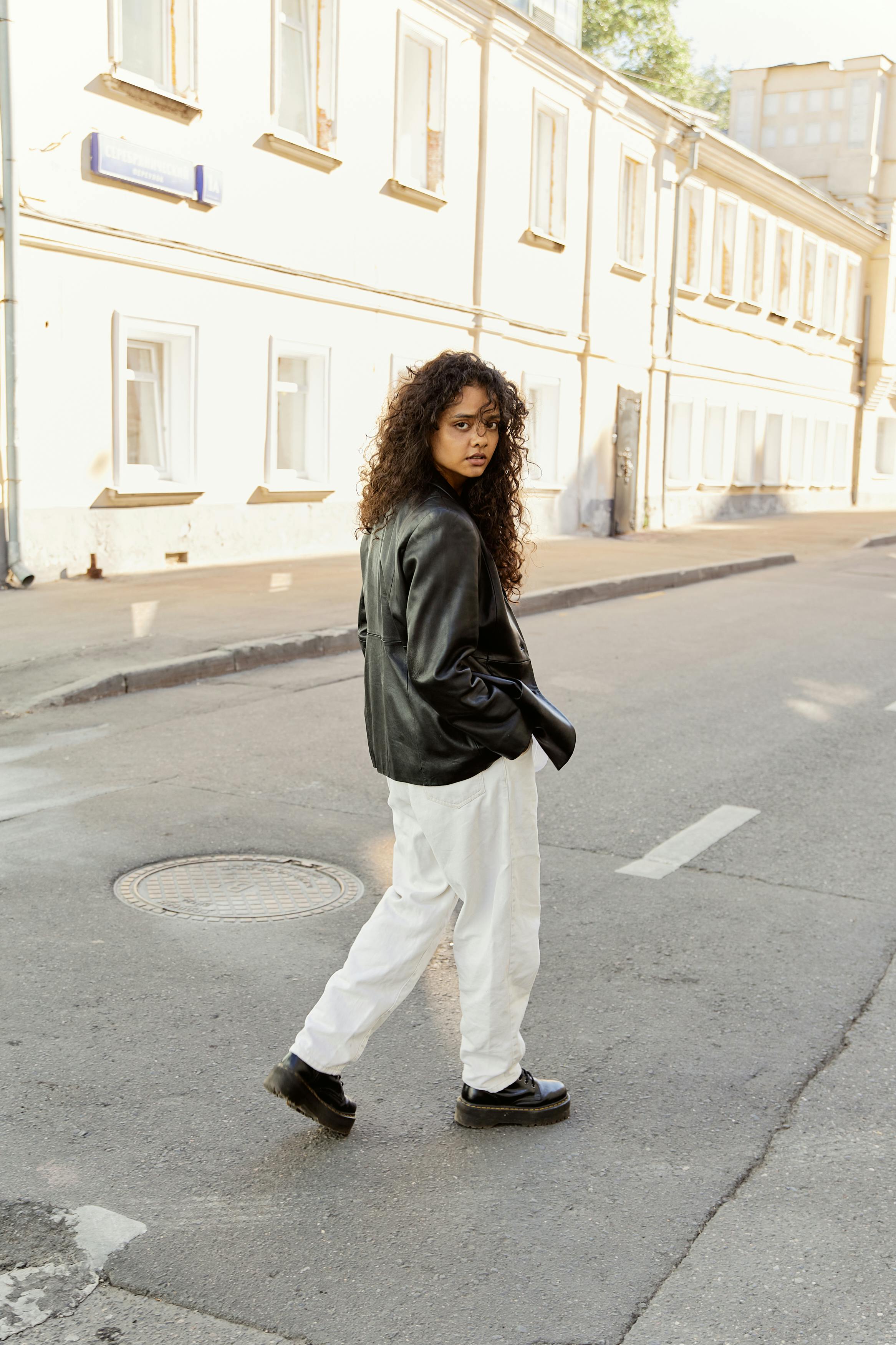 Young beautiful fashion model girl with a handbag in a black T-shirt, pants  and white sneakers poses near a white metal wall Stock Photo