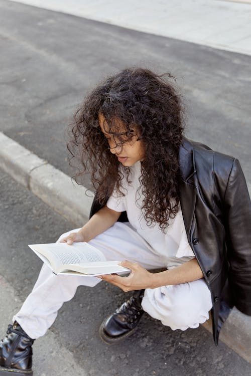 A Woman Sitting on the Walk While Reading a Book