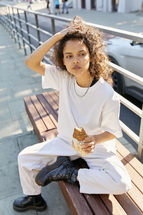 Free Casual scene of a woman sitting on a bench eating a sandwich, enjoying the outdoors. Stock Photo
