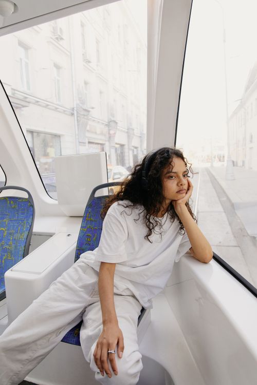 Free A young woman in casual attire relaxes inside a modern tram with large windows and urban scenery. Stock Photo