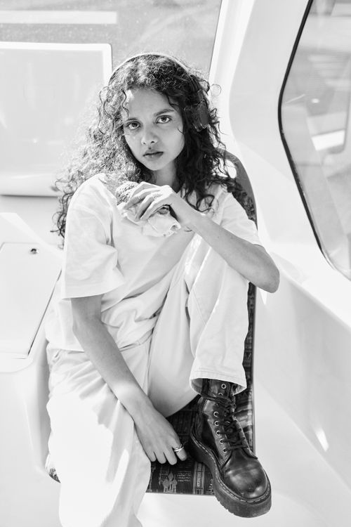 Free Black and white portrait of a young woman riding a bus, deep in thought, framed by a large window. Stock Photo