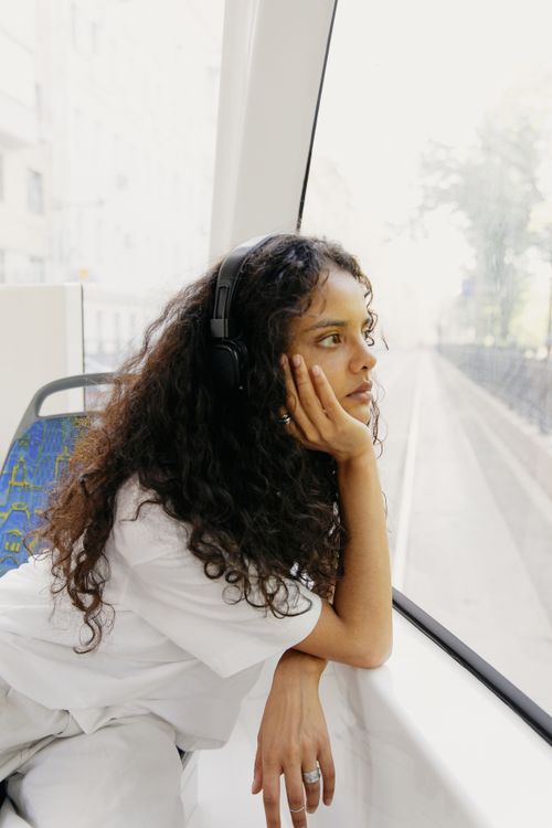 Free Woman with headphones gazing out a window on public transport, lost in thought. Stock Photo