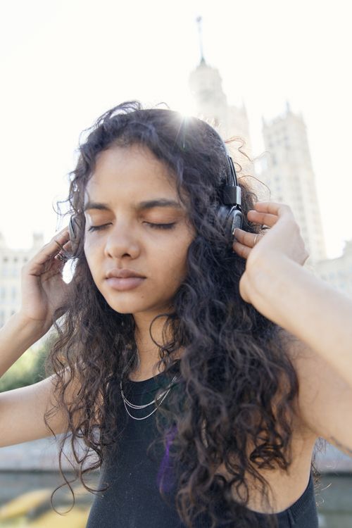 Free Young woman with headphones enjoying music outdoors, eyes closed, in a relaxed state. Stock Photo